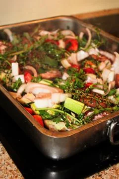 The corner of a roasting pan full of vegetables and herbs Stock Photos