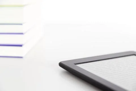 Corner of a stack of books and an electronic reader with a text on the screen 스톡 사진