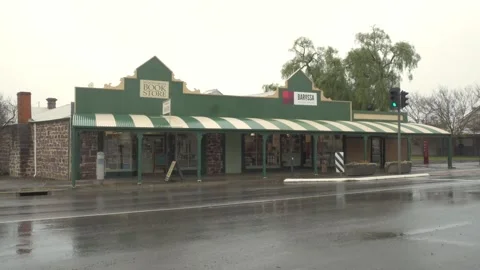 Corner Storefront Under Striped Green-and-White Awning Along Wet Street Of Stock Footage 333658866