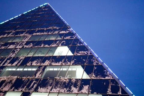 The corner of a triangular, glass, office, modern building with luminous wind Stock Photos
