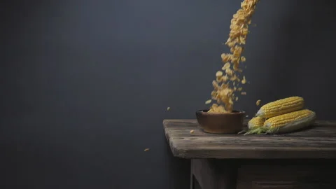 Cornflakes fall into a bowl on a wooden table. ears of corn lie nearby. Stock Footage 159091180