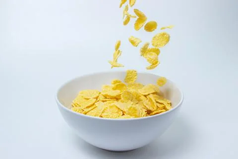 Cornflakes fall into a plate on a white background.  Stock Photos