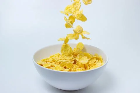 Cornflakes fall into a plate on a white background.  Stock Photos