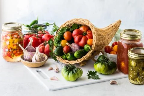 A cornucopia filled with garden vegetables and surrounded by preserves. Stock Photos