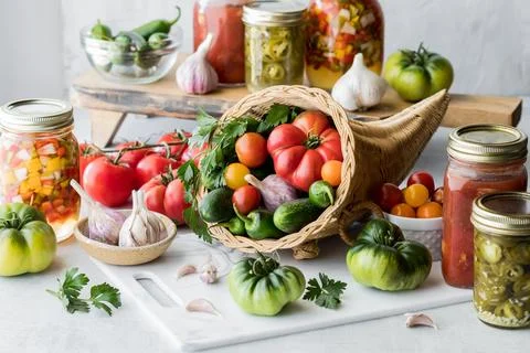 A cornucopia filled with vegetables with vegetable preserves and produce around. Stock Photos