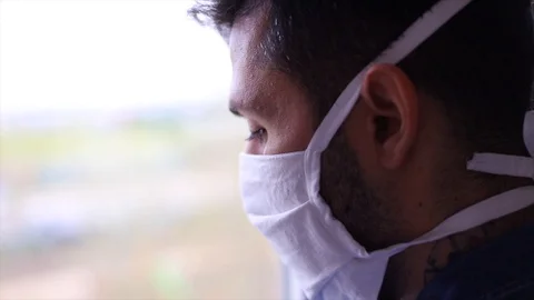 Corona virus. Sick man with crown virus looking out the window and wearing pr Stock Footage 128984553
