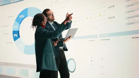 Corporate managers evaluate fiscal performance metrics on digital wall Stock Photos