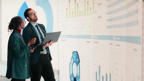 Corporate managers evaluate fiscal performance metrics on digital wall Stock Photos