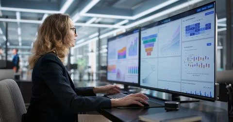 Corporate Woman Studying Multiple Computer Screens In Office, Analyzing Data. 写真素材