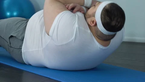 Corpulent male with fat belly doing sit ups exercise on mat home fitness class