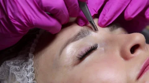 Correction and shaping of women's eyebrows in a beauty salon with a sharp knife. Stock Footage 156236812