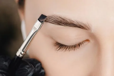 Correction and tint of eyebrows, master applies brush to woman marking on brow Stock Photos