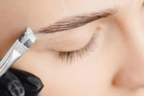 Correction and tinting eyebrows, master applies brush to woman marking on brow Stock Photos