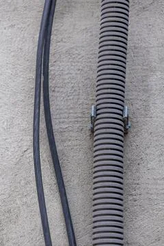 Corrugated conduit pipe with secured electrical cables on textured wall Stock Photos