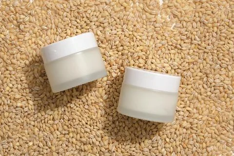 Cosmetic jars with empty label placed on a pile of wheat seeds. Flat lay for  Stock Photos
