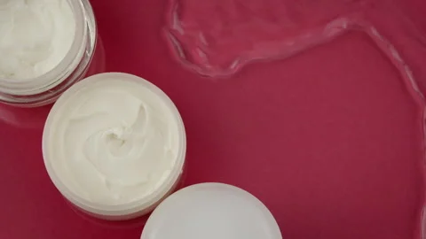 Cosmetic jars with moisturizing cream in clean water splash on red background Video stock 154875445