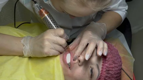 Cosmetic procedure of permanent make-up of lips. Woman-cosmetician applies the Видео 98097527