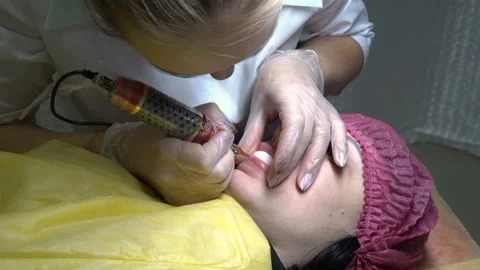 Cosmetician does permanent makeup of the lips of the woman who lies on a couch  스톡 동영상 99691162