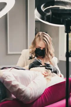 Cosmetologist applying permanent make up eyebrows for a client Stock Photos