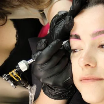 Cosmetologist applying permanent make up eyebrows for a client in a salon Stock Photos