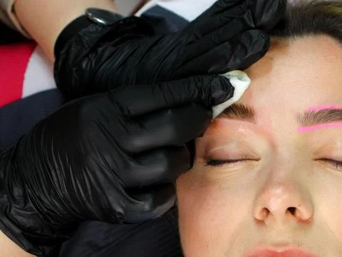 Cosmetologist applying permanent make up eyebrows for a client in a salon Stock Photos