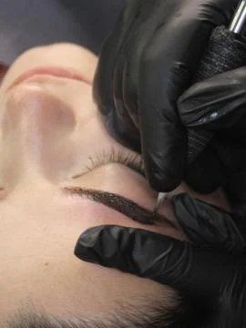 Cosmetologist applying permanent make up eyebrows for a client in a salon Stock Photos