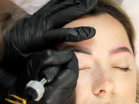 Cosmetologist applying permanent make up eyebrows for a client in a salon Stock Photos