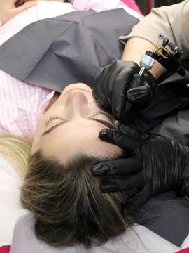 Cosmetologist applying permanent make up eyebrows for a client in a salon Foto stock