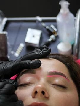 Cosmetologist applying permanent make up eyebrows for a client in a salon Stock Photos