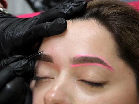 Cosmetologist applying permanent make up eyebrows for a client in a salon Stock Photos
