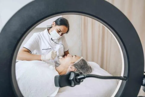 A cosmetologist blogger performs a procedure using a ring lamp to show Stock Photos