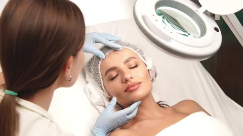 Cosmetologist checking female face under lamp in beauty cabinet Video stock 143162576