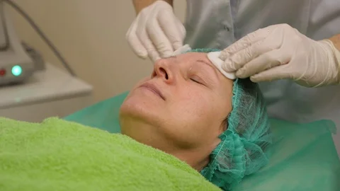 Cosmetologist cleans elder woman's face with sponges before cosmetic procedures Stock Footage 102400771