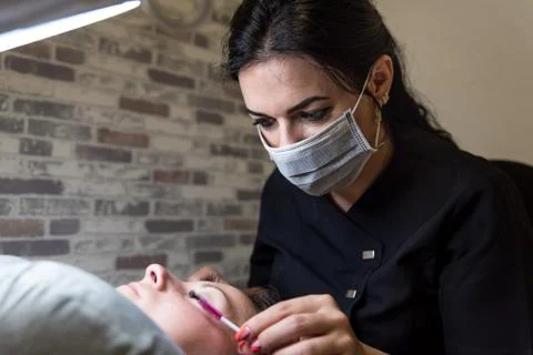 Cosmetologist is combing eyelashes of client using disposable eyelash brush Stock Photos