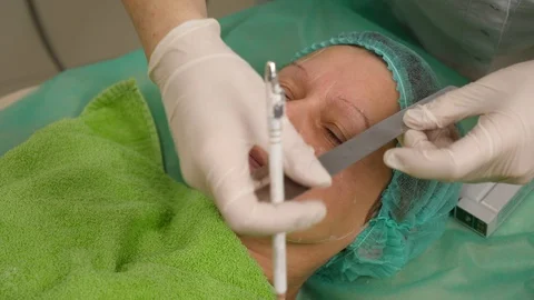 Cosmetologist draws lines elder on woman's face before face lifting procedure at Stock Footage 102400718