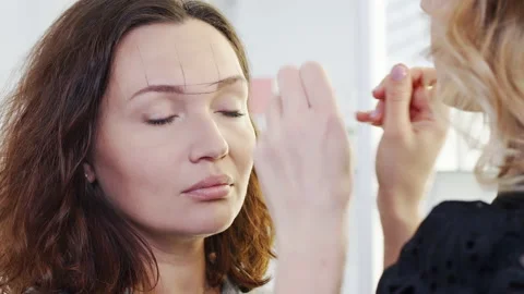 Cosmetologist forms the eyebrow line with a black thread on a female face. Ma Stock Footage 219932863