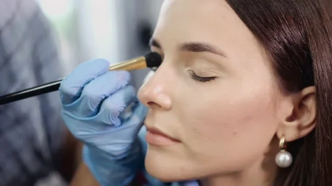 Cosmetologist in gloves applies eyeshadows on client face Stock Footage 140051634