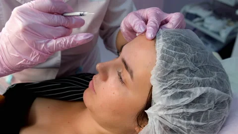 Cosmetologist makes injection of botulinum in woman's forehead, side view. Stock Footage 146318010