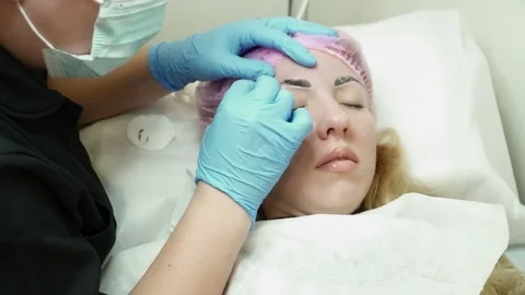 Cosmetologist is making an eyebrow permanent makeup for a woman in salon Stock Footage 74215117