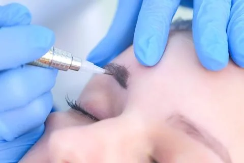 Cosmetologist making eyebrows microblading procedure in beauty salon for woman. Stock Photos