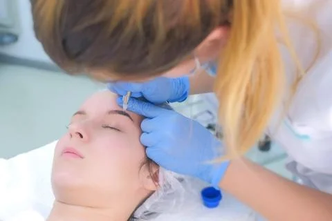 Cosmetologist making eyebrows microblading procedure in beauty salon for girl. Stock Photos