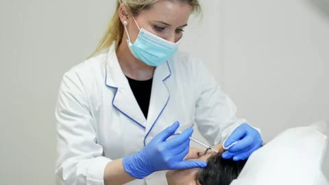 Cosmetologist making injection. She is holding syringe. Woman is receiving Stock Footage 145695064