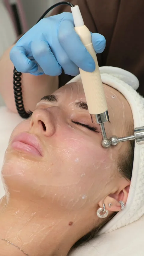 Cosmetologist performing a microcurrent therapy facial rejuvenation treatment Stock Footage 308989259