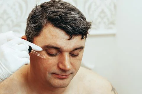 The cosmetologist performs anti-aging procedures, applies serum with hyaluronic Stock Photos