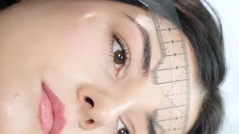 A cosmetologist performs a permanent eyebrow make-up procedure using a special Stock-Footage 250384648