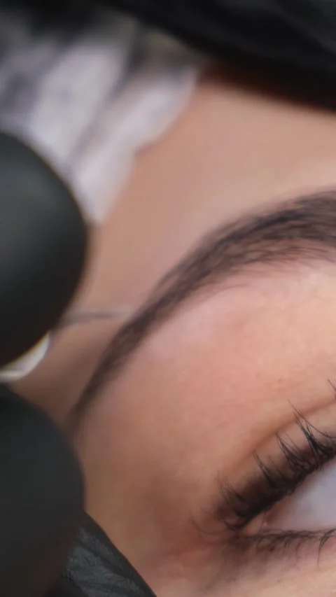 The cosmetologist performs the procedure of permanent makeup of the eyebrows in Stock Footage 250440016