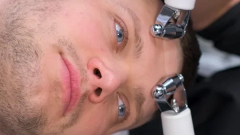 A cosmetologist performs a rejuvenating massage on a man's face using modern Stock Footage 250356473