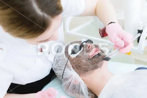 The cosmetologist in pink gloves with a brush applies a carbon mask for peeling Stock Photos