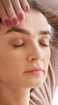 Cosmetologist plucks client eyebrows by thread in the beauty salon Stock Photos