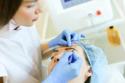 Cosmetologist shaping eyebrows before microblading. Stock Photos